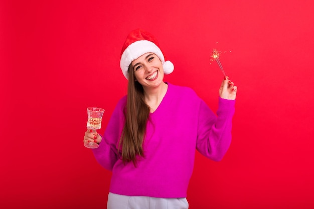 Święta Bożego Narodzenia Piękna brunetka w czapce Świętego Mikołaja pije szampana i trzyma ognie