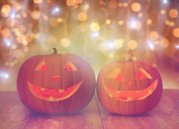 święta, halloween i koncepcja dekoracji - zbliżenie rzeźbionych dyni z uśmiechniętymi buźkami na stole nad światłami