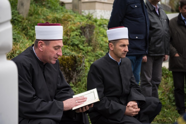 Zdjęcie święta księga koranu czytana przez imama na islamskim pogrzebie z białymi kamieniami kciuka na tle cmentarza