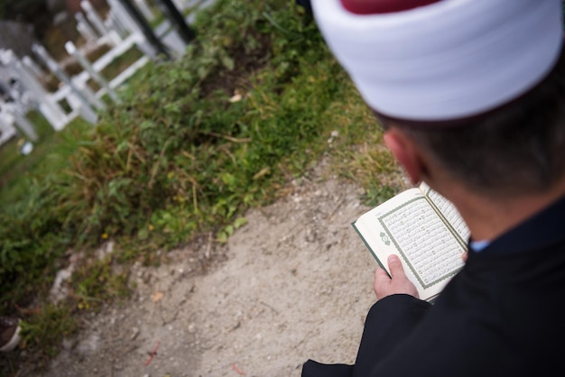 święta księga koranu czytana przez imama na islamskim pogrzebie z białymi kamieniami kciuka na tle cmentarza