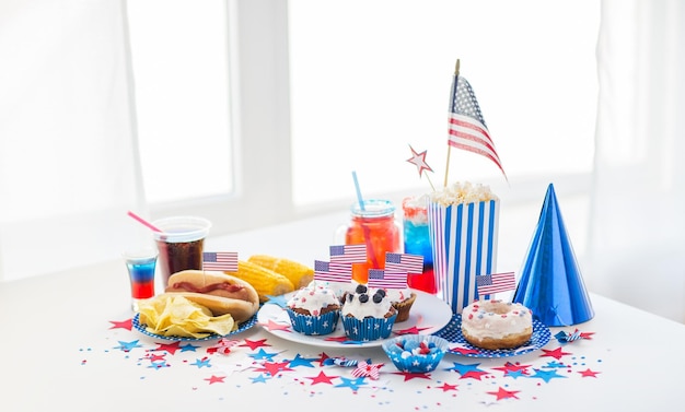 święta narodowe, celebracja, jedzenie i koncepcja patriotyzmu - zbliżenie hot doga z dekoracją flagi amerykańskiej, chipsy ziemniaczane i napoje 4 lipca na imprezie domowej w dzień niepodległości