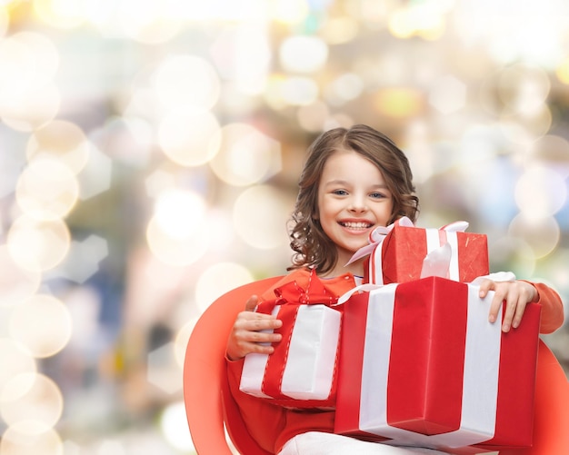 święta, prezenty, boże narodzenie, dzieciństwo i koncepcja ludzi - uśmiechnięta dziewczynka z pudełkami prezentów na tle światła