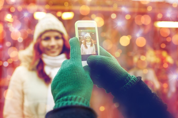 Zdjęcie Święta, zima, święta, technologia i koncepcja ludzi - szczęśliwa para turystów w ciepłych ubraniach robi zdjęcie smartfonem na starym mieście