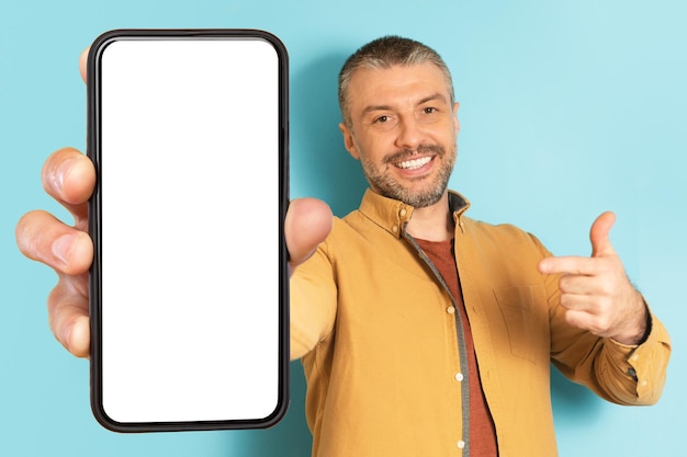Świetna oferta Podekscytowany dojrzały mężczyzna trzymający i wskazujący palcem duży telefon komórkowy z białym ekranem promującym aplikację lub stronę internetową