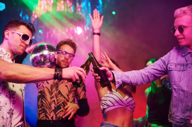 Świętowanie i pukanie do butelek z alkoholem Młodzi ludzie bawią się w nocnym klubie z kolorowymi światłami laserowymi