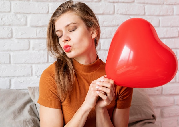 Świętowanie walentynek dzień ślubu i miłości dzień kobietPiękna kobieta trzymająca balon w kształcie czerwonego serca siedząca w łóżku