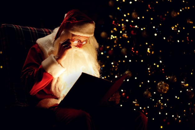 Zdjęcie Święty mikołaj czytając magiczną książkę siedząc w ciemnym pokoju