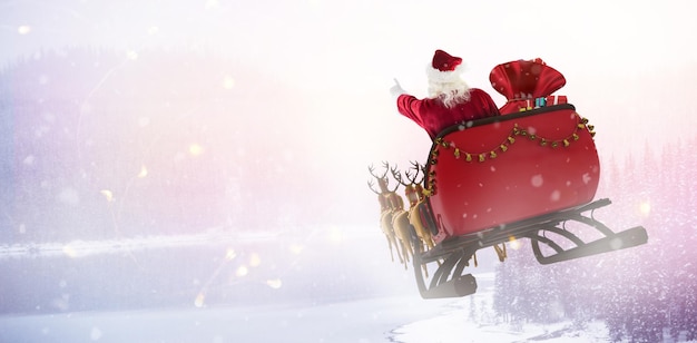 Święty Mikołaj jedzie na saniach z pudełkiem na ośnieżone sosny nad jeziorem