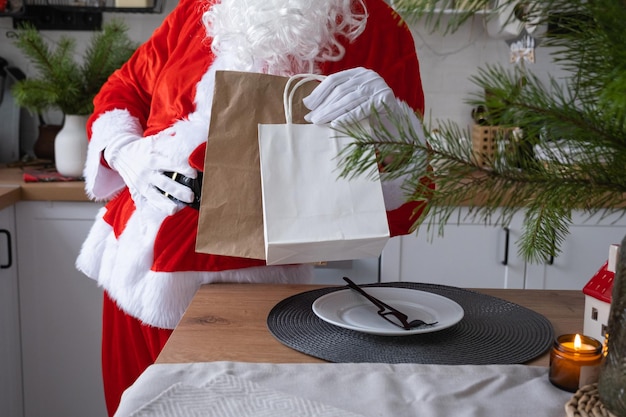 Święty Mikołaj kładzie go na kuchennym stole i zabiera papierowe torby z prezentami rzemieślniczymi, domowymi ciastami i dostawą żywności Recykling opakowań na zakupy Ręcznie robiona dostawa na Boże Narodzenie i Nowy Rok