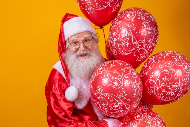 Święty Mikołaj na żółtym tle trzymając czerwone balony.