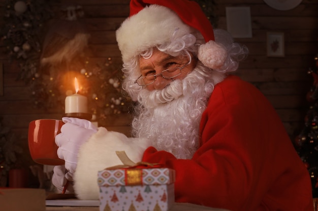 Święty Mikołaj odpoczywa w wygodnym fotelu przy kominku w domu.