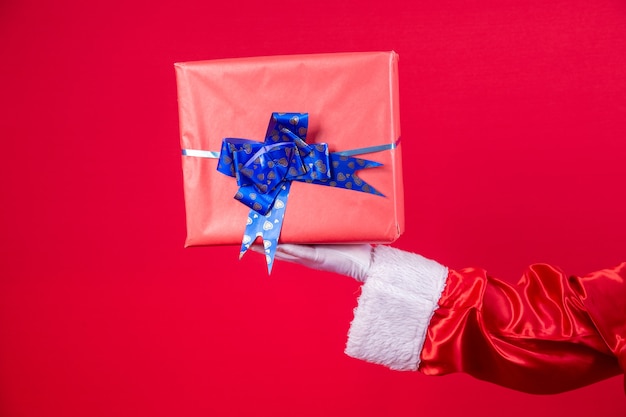 Święty Mikołaj ręka trzyma pudełko na prezent Boże Narodzenie na czerwonym tle.