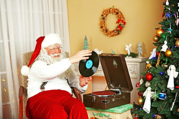 Święty Mikołaj siedzi w wygodnym fotelu w pobliżu retro gramofonu w domu