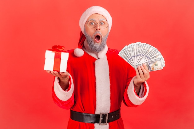 Święty mikołaj stojący z fanem dolarów i pudełko z prezentem świątecznym.