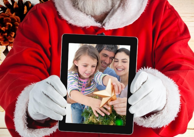 Święty Mikołaj trzyma cyfrowy tablet ze zdjęciem świątecznej rodziny