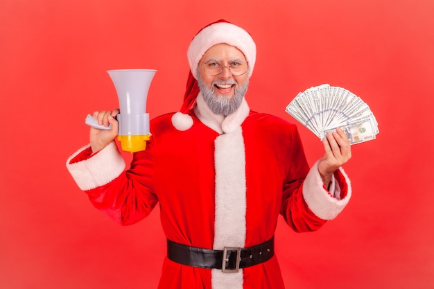 Święty Mikołaj Trzyma Fan Banknotów I Megafonów, Patrząc Na Kamery Z Szczęśliwym Wyrazem Twarzy.