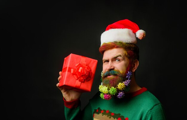 Święty mikołaj trzyma prezent sylwestrowy pudełko na prezent życzę wesołych świąt uśmiechnięty mężczyzna w santa hat