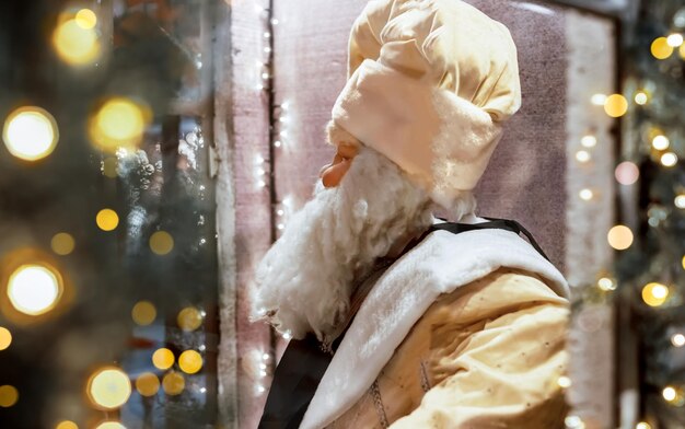 Święty Mikołaj w stylu retro siedzi za witryną sklepową ze światłami na Boże Narodzenie