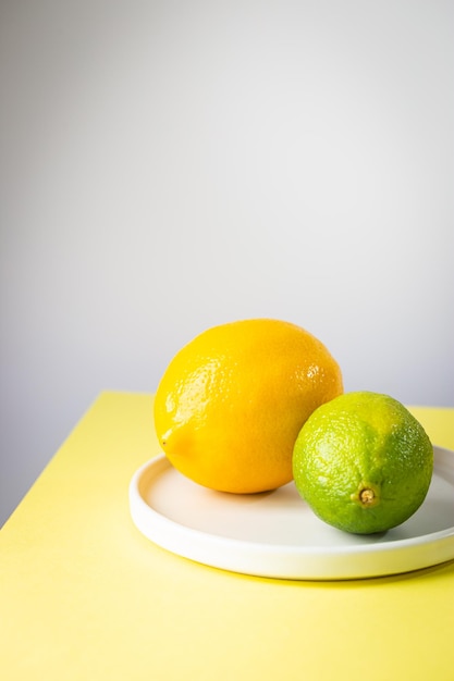 Świeża cytryna i limonka na talerzu na dwukolorowym tle żółtej i białej minimalistycznej kompozycji
