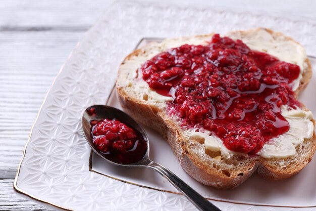 Zdjęcie Świeża grzanka z domowym masłem i dżemem malinowym na talerzu na drewnianym tle