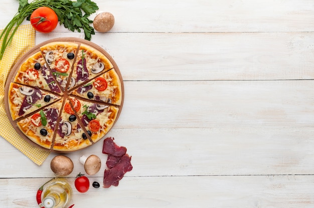 Świeża pizza w rustykalnym włoskim stylu z suszonymi oliwkami, pieczarkami i trzema rodzajami sera na jasnym drewnianym tle