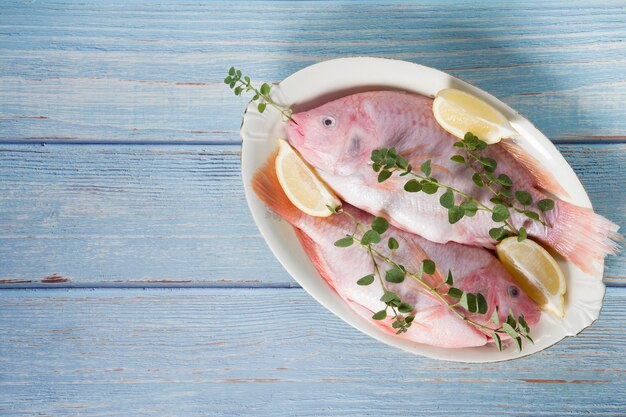 Świeża różowa tilapia leży na tacce otoczonej żółtymi cytrynami