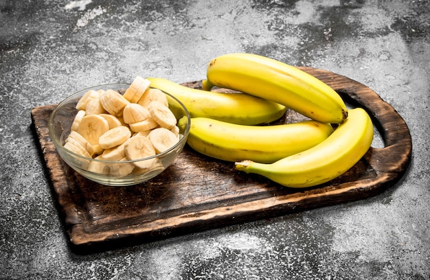 Zdjęcie Świeże banany z kawałkami pokrojonych bananów w misce. na rustykalnym stole.