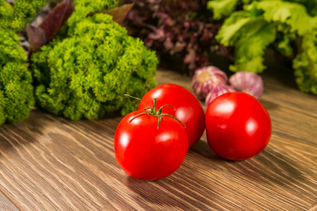 Świeże, dojrzałe pomidory na drewnianym stole z zieloną sałatą na ścianie Świeże warzywa. Pyszne wegetariańskie jedzenie. Sałatka.