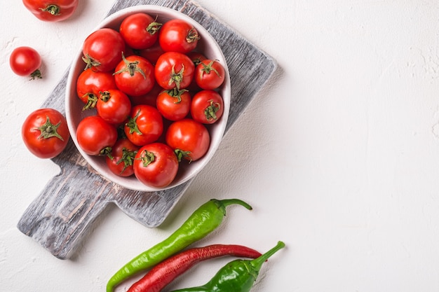 Świeże, dojrzałe pomidory w misce na starej drewnianej desce do krojenia z ostrą papryką chili