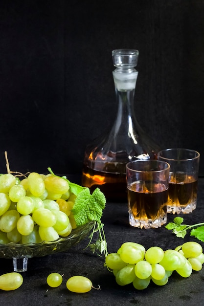 Świeże dojrzałe winogrona w misce z owocami i karafce oraz dwie szklanki z sokiem winogronowym na czarnym tle