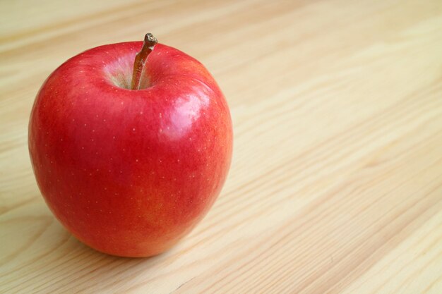 Świeże dojrzałe, żywe czerwone jabłko na jasnobrązowym drewnianym stole z miejscem na kopię
