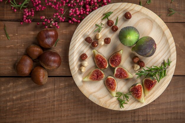 Zdjęcie Świeże figi na drewnianym talerzu z orzechami laskowymi, czerwoną papryką i rozmarynem