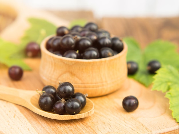 Świeże jagody czarnej porzeczki w misce na drewnianym stole w pobliżu zielonych liści Soczyste owoce naturalnej porzeczki Czarna porzeczka