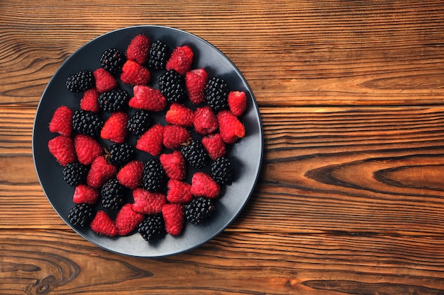 Świeże jagody organiczne lato wymieszać w okrągły czarny stół na tle ciemnego stołu drewnianego. Maliny i jeżyny. Widok z góry