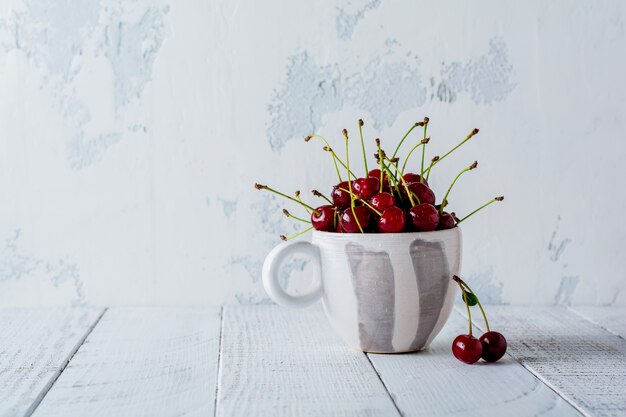 Świeże jagody wiśni w vintage ceramiczny kubek na jasnej drewnianej starej powierzchni.