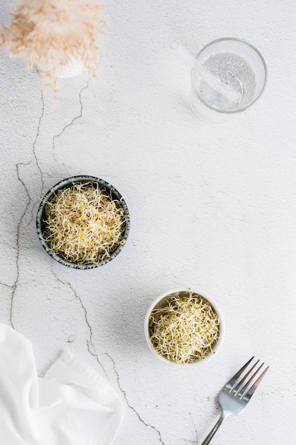 Zdjęcie Świeże kiełki koniczyny i lucerny do jedzenia w misce i szklanka wody na stole