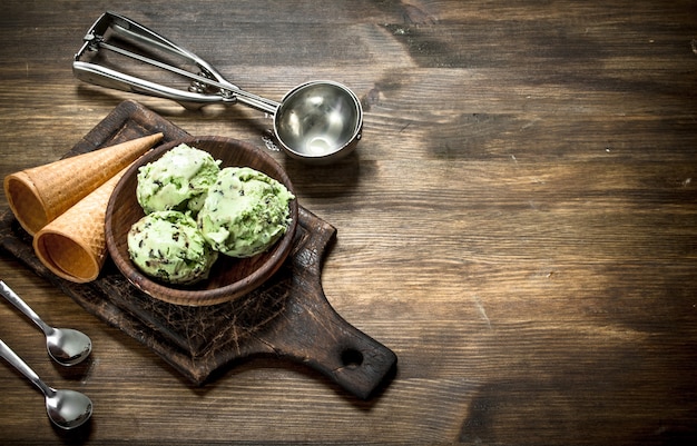 Świeże lody pistacjowe w misce z kubkami waflowymi na drewnianym stole