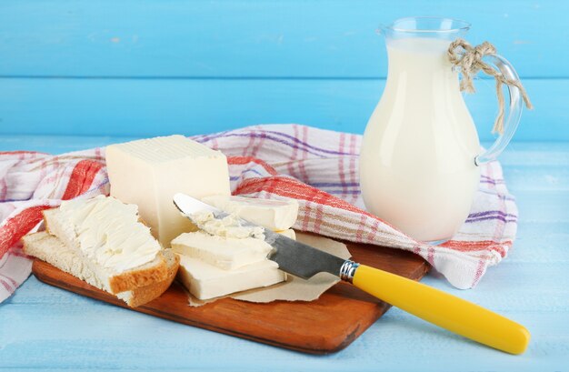 Zdjęcie Świeże masło na desce do krojenia i dzbanek z mlekiem, na kolorowym drewnianym stole