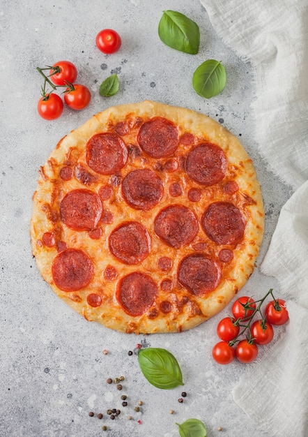 Świeże okrągłe pieczone włoska pizza Pepperoni z pomidorami z bazylią na tle jasnego stołu kuchennego. Miejsce na tekst