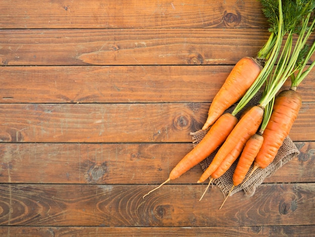 Świeże organiczne marchewki z zielonymi liśćmi na drewnianym tle Warzywa