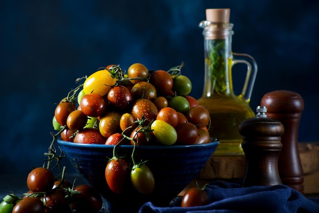 Świeże organiczne pomidorki koktajlowe na gałęzi, kolorowe sezonowe pomidory w misce na ciemnym tle, selektywne focus