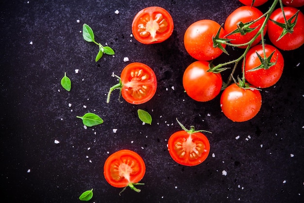 Świeże organiczne pomidorki koktajlowe z bazylią i solą morską na ciemnym tle