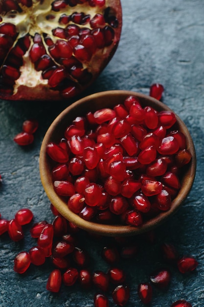 Świeże organiczne soczyste nasiona granatu w drewnianej misce na ciemnym tle kamienia