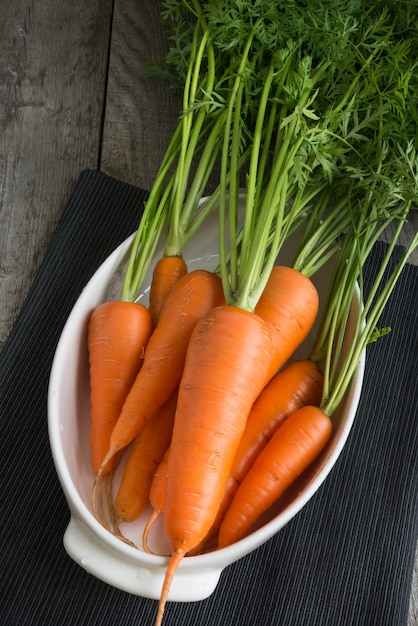 Świeże organicznie marchewki z zielonymi wierzchołkami w bielu talerzu na stole. Skopiuj miejsce. Widok z góry.