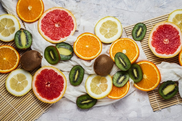 Świeże owoce tropikalne, grejpfrut, cytryna, pomarańcza, kiwi na jasnym tle kamienia.