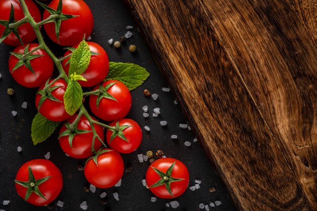 Świeże pomidory czereśniowe na czarnym tle z przyprawami.