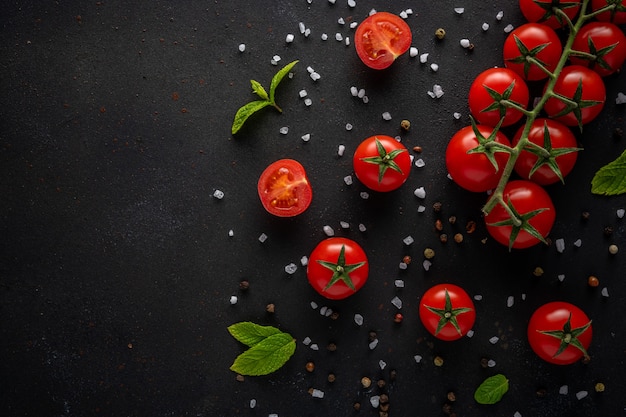 Świeże pomidory czereśniowe na czarnym tle z przyprawami