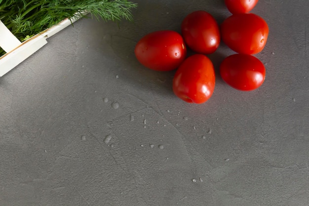 Świeże pomidory i koperek z natką pietruszki w koszu winorośli leżą na szarym stole