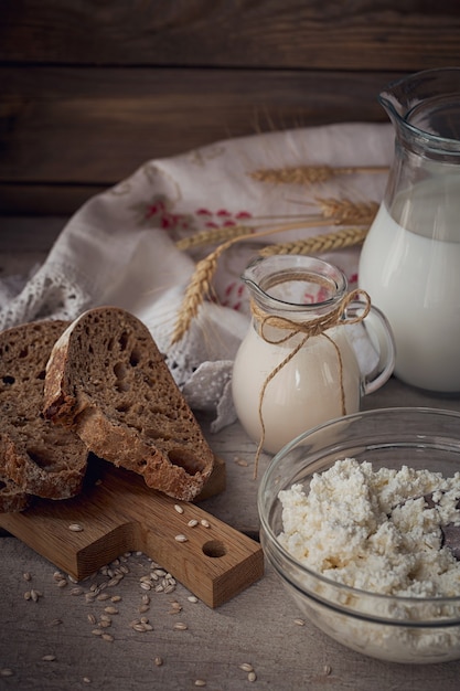 Świeże produkty mleczne. Mleko, twarożek, śmietana, domowy chleb wieloziarnisty i pszenica na rustykalne drewniane tła. Koncepcja mleczarstwa ekologicznego.