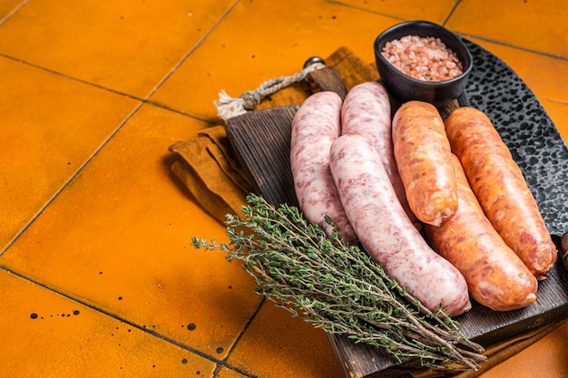 Zdjęcie Świeże surowe kiełbaski mięsne bratwurst i chorizo na drewnianej desce pomarańczowe tło widok z góry kopiuj przestrzeń